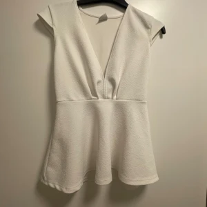 Vit topp från Gina Tricot - Säljer en stilren vit topp från Gina Tricot med djup v-ringning och korta ärmar. Toppen har en lätt utställd passform som ger en fin silhuett.