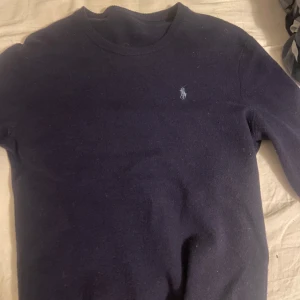 Mörkblå tröja från Ralph Lauren - Snygg mörkblå tröja från Ralph Lauren med det klassiska logotypbroderiet på bröstet. Tröjan har en rund halsringning och långa ärmar, perfekt för en stilren look.