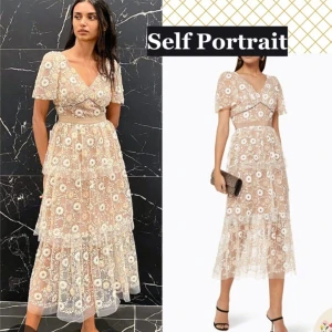 Blommig spetsklänning från Self Portrait - Elegant blommig spetsklänning från Self Portrait med v-ringad hals och korta ärmar. Klänningen har en omlott-design och volanger som ger en romantisk känsla. Perfekt för speciella tillfällen.