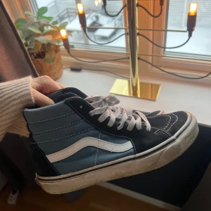  sneakers från Vans - Säljer ett par klassiska Vans sneakers i svart och blått med vit sula och snörning. Skorna har den ikoniska sidostripen i vitt och är perfekta för en avslappnad stil.