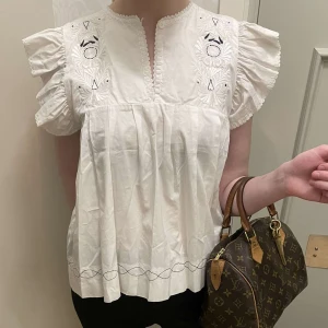 Vit blus från By Malene Birger - Säljer en söt vit blus från By Malene Birger med broderade detaljer och korta volangärmar. Blusen har en v-ringad hals och fina veck framtill. Perfekt för en stilren look. Sjukt snygg och inga defekter! Sjukt bra kvalitet💕💕 köpt för 1600!