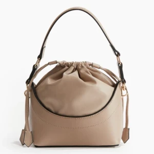 Beige axelväska med dragsko - Snygg beige axelväska i syntetmaterial med dragsko upptill. Väskan har en justerbar axelrem och en kortare handrem för olika bärstilar. Perfekt för en stilren look. Helt ny väska med lappen på! Pris kan diskuteras!! Hör av dig vid minsta lilla 🥰