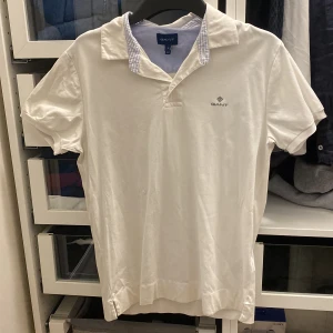 Vit kortärmad pikétröja från GANT - Säljer en stilren vit pikétröja från GANT i storlek S. Tröjan har korta ärmar och en klassisk krage med diskret logotyp på bröstet. Perfekt för en avslappnad och snygg look. Tröjan är knappt använd och väldigt gott skick!