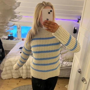 Randig stickad tröja från Vero Moda - Mysig stickad tröja från Vero Moda i beige med blå ränder. Tröjan har en hög krage och långa ärmar, perfekt för kyliga dagar. Den hade ett litet hål när ja köpte den som ja har lagat, Men syns knappt nu (se på bild 3)
