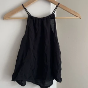 Svart ärmlös linnetopp - Snygg svart ärmlös linnetopp med smala axelband. Perfekt för varma sommardagar eller som ett lager under en jacka. Enkel och stilren design som passar till det mesta. (EGNA BILDER PRIVAT) 