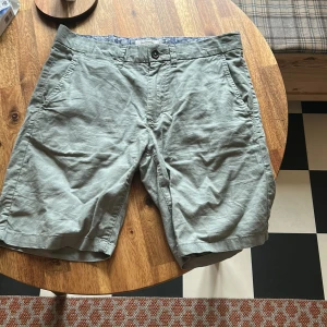 Gröna shorts från Dressmann - Snygga gröna shorts från Dressmann med dragkedja och knapp framtill. De har en klassisk passform och är perfekta för varma dagar. Insidan har ett mönstrat foder som ger en extra touch av stil.