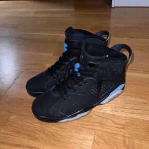 Jordan 6 Retro - Snygga svarta sneakers med blå detaljer och snörning. Perfekta för en sportig look med en klassisk design. Skorna har en högre modell och är dekorerade med den ikoniska loggan.