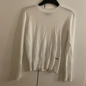 Vit tröja från Marine - Säljer en stilren vit tröja från Marine i storlek XS. Tröjan har långa ärmar och en rund halsringning. Den är dekorerad med en liten metallbricka med märkesnamnet på framsidan. Perfekt för en klassisk och elegant look.
