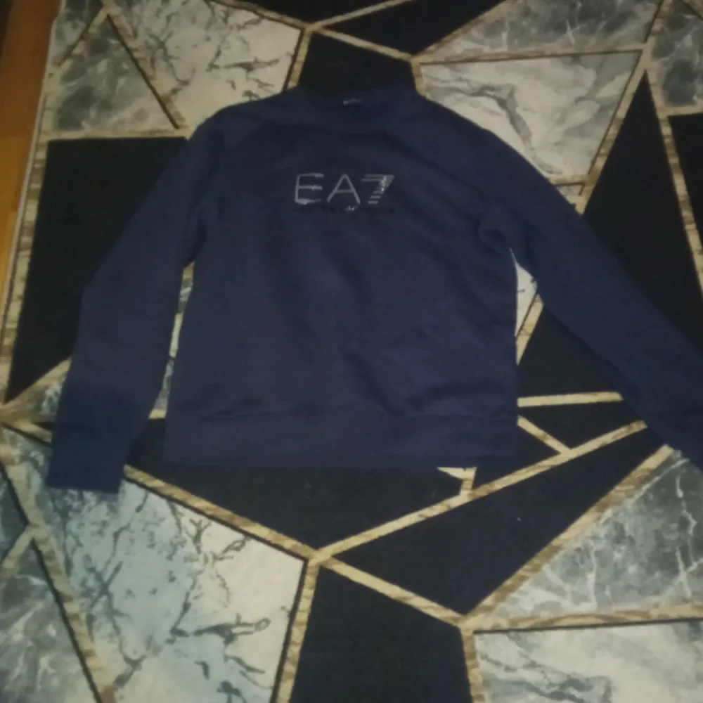 Säljer en stilren mörkblå tröja från Emporio Armani med EA7-logga på bröstet. Tröjan har långa ärmar och en klassisk passform. Perfekt för en avslappnad och trendig look.. Neuletakit & Villapaidat.