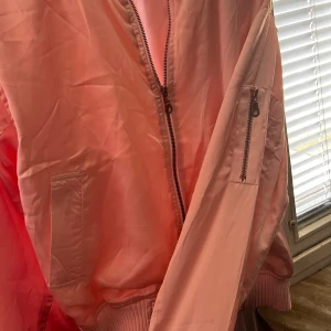 Rosa bomberjacka från The Black Label Collection - Snygg rosa bomberjacka från The Black Label Collection med dragkedja framtill och praktiska fickor på ärmen. Perfekt för en cool och avslappnad stil. Jackan har ribbade muddar vid hals och ärmslut.