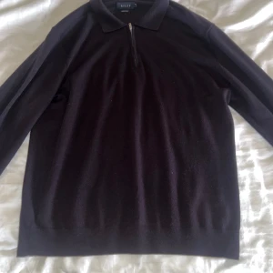 Svart tröja från Riley - Snygg svart tröja från Riley med dragkedja vid halsen och klassisk krage. Perfekt för en stilren look. Tröjan har långa ärmar och är tillverkad i ett mjukt material.