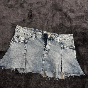 Jeanskjol från Weekday - Snygg volang jeanskjol från Weekday i en klassisk blå denim. Kjolen har en rå kant nertill och en cool, avslappnad stil. Perfekt för en trendig look.