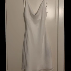 Vit klänning - Snygg vit klänning med smala axelband och en elegant, enkel design. Perfekt för sommarens varma dagar eller en speciell kväll. Klänningen har en smickrande passform och är tillverkad i ett lätt material som ger en luftig känsla. Helt oanvänd. Inte heller för genomskinlig. 