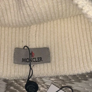 Vit stickad mössa från Moncler - Säljer en stilren vit stickad mössa från Moncler. Mössan har en broderad logotyp framtill och är perfekt för kyliga dagar. Den är ribbad och ger en skön passform.