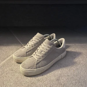 Grå sneakers i mocka - Snygga gråa sneakers i mocka med snörning. Perfekta för en stilren look. Skorna har en robust sula och en klassisk design som passar till det mesta. En liten skada i hälen men inget man känner av eller så, det är unikt matrial nått swued/mocka liknande