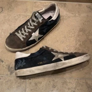 Svarta sneakers med stjärndetalj - Snygga svarta sneakers från Golden Goose med en vit stjärna på sidan. Skorna har en klassisk snörning och en vit sula. Perfekta för en avslappnad stil.