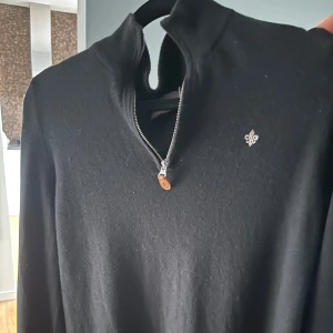 Svart Morris tröja med dragkedja Storlek M - Snygg svart tröja med dragkedja och en liten broderad detalj på bröstet. Perfekt för en stilren look. Tröjan har långa ärmar och en hög krage.