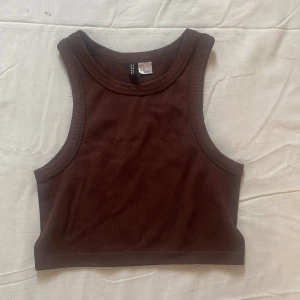 Brun ribbad linnetopp från Divided/H&M - Snygg brun ribbad linnetopp från Divided. Perfekt för en avslappnad stil med sin ärmlösa design och croppade längd. Passar utmärkt till jeans eller kjol på sommaren. Använd en gång.