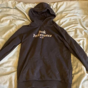 Mörkblå hoodie från Peak Performance - Säljer en mörkblå hoodie från Peak Performance med tryck på framsidan. Den har en klassisk design med huva och en stor ficka framtill. Perfekt för en avslappnad stil.