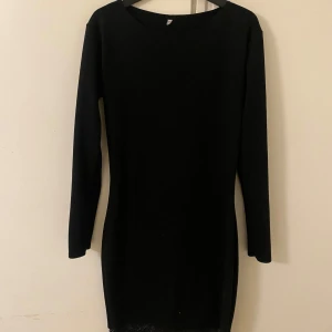 Svart klänning med spetsdetalj - Elegant svart klänning med långa ärmar och spetsdetalj vid fållen. Perfekt för en stilren look.