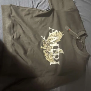 Svart tröja från Amiri med örntryck - Snygg svart tröja från Amiri med ett stort tryck av en örn och märkesnamnet på framsidan. Tröjan har en klassisk passform och rund halsringning. Perfekt för en stilren look.