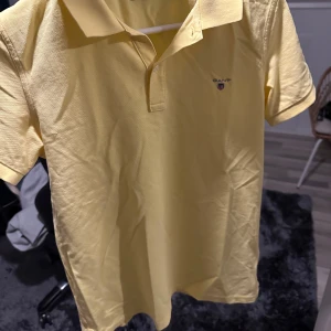 Gul pikétröja från GANT - Snygg gul pikétröja från GANT med klassisk krage och knappdetalj framtill. Perfekt för en avslappnad men stilren look. Passar bra till både jeans och chinos.                                                                            Storlek 164 cm vilket motsvarar xs. Obs! Tröjan strycks innan den skickas👍