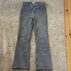 Grå byxor från MNG - Snygga grå byxor från MNG med bootcut-stil och hög midja. Byxorna har framfickor och en knappdetalj i midjan. Perfekta för en stilren look.
