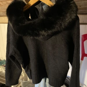 Svart stickad tröja med faux fur - Snygg svart stickad cardigan med dragkedja och en lyxig pälsdetalj runt kragen. Perfekt för att hålla sig varm och stilren under kyliga dagar. Tröjan har långa ärmar och en bekväm passform. Helt oanvänd. Köpt för 1200 på Alessas hemsida💗