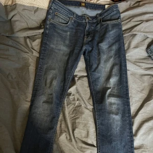Blå jeans från Lee - Snygga blå jeans från Lee med klassisk femficksdesign och en bekväm passform. De har en dragkedja och knapp framtill samt en diskret Lee-logga på bakfickan. Perfekta för en avslappnad stil.