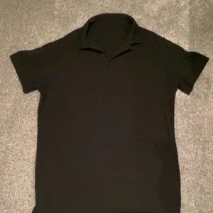 Svart kortärmad pikétröja - Snygg svart pikétröja med korta ärmar. Perfekt för en stilren och avslappnad look. Tröjan har en klassisk krage och är tillverkad i ett bekvämt material. Passar dig runt 170