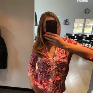 Mönstrad blus från Odd Molly - Säljer en snygg blus från Odd Molly med ett livligt rött och rosa mönster. Blusen har långa ärmar och en v-ringad design som ger en stilren look. Perfekt för att liva upp garderoben! 🌸