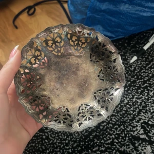 Dekorativ skål i silver - Elegant dekorativ skål i silver med utskurna mönster längs kanterna. Perfekt som prydnad eller för servering av små föremål. Skålen har en vacker, antik finish som ger den en klassisk känsla.