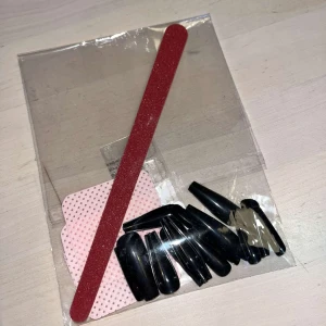 Lösnaglar - Set med svarta lösnaglar och en röd nagelfil. Perfekt för att fixa snygga naglar snabbt. Inkluderar även klisterlappar för enkel applicering och luddfria pads. Naglarna har en glansig finish och kommer i olika storlekar för att passa alla fingrar.