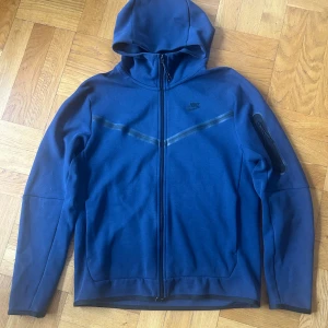 Nike tech fleece  - Säljer blå Nike tech fleece med dragkedja framtill. Tröjan är i storlek M, har normal passform och är långärmad med en praktisk ficka på ärmen. Är i väldigt gott skick!