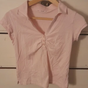 Ljusrosa kortärmad topp från H&M - Säljer en ljusrosa kortärmad topp från H&M med krage och knappar framtill. Material i bomull. Lappen på tröjan är bortklippt så storlek är okänd, skulle gissa på XS-S! Kan stryka toppen innan leverering så att den blir slät och fin.