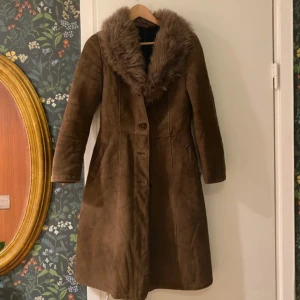 Brun mockakappa med pälsdetaljer - Otrolig Penny laine mockakappa med en lyxig pälsdetalj runt kragen. Kappan har en klassisk design med knappar framtill och långa ärmar. Perfekt för kyligare dagar när du vill känna dig både varm och stilfull ❤️‍🔥 köpt på beyond retro. Vid snabb affär kan pris diskuteras 