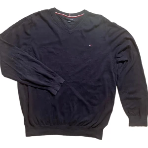 Svart tröja från Tommy Hilfiger - Säljer en stilren svart tröja från Tommy Hilfiger med v-ringning och diskret logga på bröstet. Tröjan har långa ärmar och ribbade muddar vid ärmslut och nederkant. Perfekt för en klassisk look.