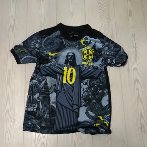 Brasiliansk fotbollströja med Neymar Jr - Snygg Brasilien fotbollströja från Nike med Neymar Jr och nummer 10 på ryggen. Tröjan har ett unikt mönster med grå och svarta nyanser samt gula detaljer. Perfekt för fans av det brasilianska landslaget.