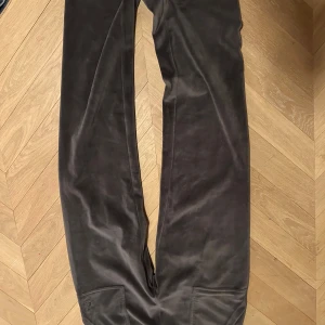 Gråa byxor från Juicy Couture - Snygga svarta byxor från Juicy Couture i mjukt material. Byxorna har en elastisk midja och en ficka med knappdetalj bak. Perfekta för en avslappnad stil.