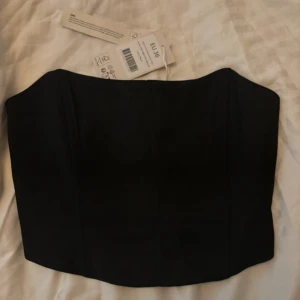 Svart korsett topp från NA-KD - Säljer en stilren svart korsett från NA-KD i storlek EU 36. Den har en smickrande passform och är perfekt för att skapa en elegant look. Korsetten har en elastisk rygg för extra komfort.