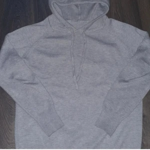 Merinoull  - Säljer en stilren grå merinoull med långa ärmar och justerbar huva. Perfekt för en avslappnad look. Den har ribbade muddar vid ärmslut och nederkant för extra komfort. Passar bra till många saker.