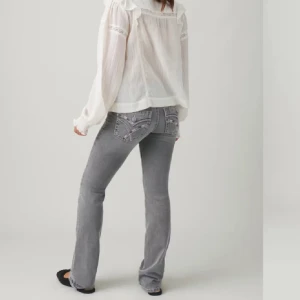 Grå jeans med broderade fickor - Snygga grå jeans med broderade detaljer på bakfickorna. De har en straight passform och är perfekta för en avslappnad stil. Kombinera med en vit blus för en chic look. Saknas en knapp 