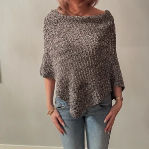 Grå stickad poncho - Säljer en mysig grå stickad poncho med en lös passform. Perfekt för kyliga dagar och ger en avslappnad look. Den har en asymmetrisk design och är lätt att matcha med jeans eller leggings. 