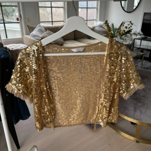 Guldglittrig bolerotopp - Säljer en glittrig bolerotopp i guld med korta ärmar och paljetter. Toppen är i strl M, men skulle även passa en S-M!💕