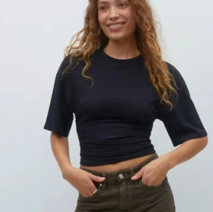 Svart t-shirt - Snygg svart t-shirt med ruched detaljer som ger en cool look. Den har en normal passform och korta ärmar, perfekt för en avslappnad stil. Materialet är mjukt och bekvämt. HELT NY med lapp kvar, men har fått smink i kragen efter proving. Men går bort i tvätten.