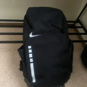 Svart ryggsäck från Nike - Säljer en svart ryggsäck från Nike med vit logga och texten 'ELITE' på axelremmarna. Ryggsäcken har flera fack och justerbara remmar för bekväm passform. Perfekt för träning eller vardagsbruk.