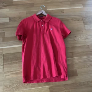 Röd pikétröja från gant  - Snygg röd pikétröja med korta ärmar och klassisk krage. Tröjan har en broderad logga på bröstet och knappar framtill. Perfekt för en avslappnad stil.