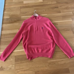 Rosa tröja från Ralph Lauren - Säljer en stilren rosa tröja från Ralph Lauren med en liten broderad logga på bröstet. Tröjan har långa ärmar och en dragkedja vid halsen. Perfekt för en avslappnad men snygg look.