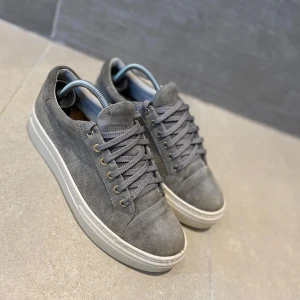 Grå vagabonds mocka - Snygga grå vagabonds sneakers i mocka med vit sula och snörning. Perfekta för en stilren look med en touch av elegans. De har en klassisk design med rund tå och diskreta detaljer.