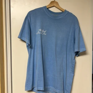 Blå t-shirt med tryck - Snygg ljusblå t-shirt med ett tryck av ett havslandskap på baksidan och texten 'The Great Adventure' på framsidan. Perfekt för en avslappnad stil.